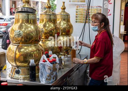 Un assistant préparant et remplissant du thé chinois fraîchement préparé dans un ensemble de distributeurs de thé chinois traditionnels en laiton pour les clients de passage dans Smith S. Banque D'Images