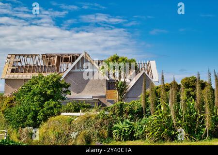 Une maison partiellement construite avec un cadre de toit visible, entourée de verdure luxuriante et de palmiers sous un ciel bleu vif avec des nuages éparpillés. Banque D'Images