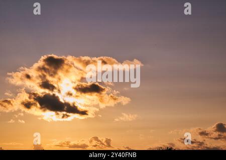 Un beau coucher de soleil aux teintes orange et jaune vibrantes, partiellement obscurci par des nuages moelleux contre un ciel dégradé passant du bleu à la tonne chaude Banque D'Images