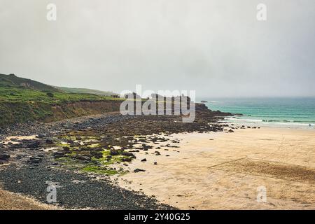 Une scène de plage sereine avec un rivage rocheux, des vagues douces et une atmosphère brumeuse. La plage de sable est parsemée de galets et d'algues, tandis que le gree Banque D'Images