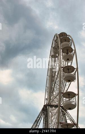 Une vue rapprochée d'une grande roue contre un ciel nuageux, mettant en valeur sa structure et ses cabines. Banque D'Images