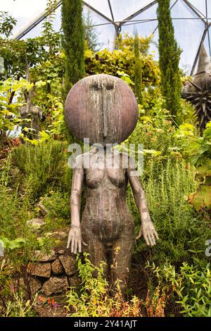 Une sculpture unique d'une figure humanoïde avec une tête ronde et un corps élancé, entouré de verdure luxuriante et de plantes. La figure semble être faite de Banque D'Images