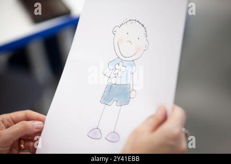 Gros plan de la main d'une femme montrant le dessin d'un enfant d'un garçon heureux tenant une fleur. Banque D'Images