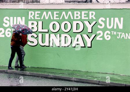 Un couple passe devant une murale pendant un jour de pluie dans la région de Bogside avant le 20e anniversaire du massacre du dimanche sanglant, le 24 janvier 1992 à Londonderry, en Irlande du Nord. Banque D'Images