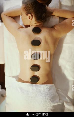 Temps de soins. Vue supérieure de la femme détendue dans le salon de spa ayant massage aux pierres chaudes et la pose sur la table de massage. Banque D'Images