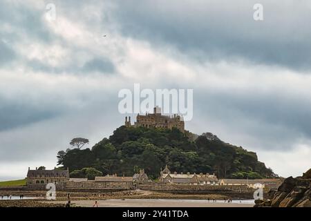 Une vue panoramique sur un château sur une colline entourée de verdure luxuriante, avec une plage de sable au premier plan et un ciel nuageux au-dessus. Banque D'Images