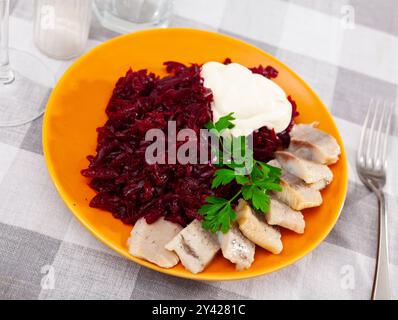 Salade de hareng appétissante avec betteraves, crème sure et persil dans une assiette blanche Banque D'Images