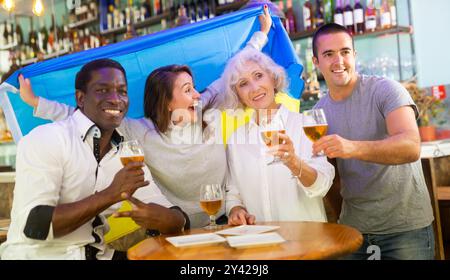 Enthousiastes fans de football masculin et féminin célébrant la victoire du championnat, agitant le drapeau de l'Ukraine dans le pub Banque D'Images