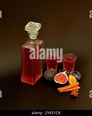 Liqueur aux prunes et aux figues à la cannelle et à l'anis, alcool maison en verrerie en cristal, épices et fruits mûrs sur fond noir. Gros plan. Banque D'Images