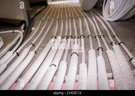 Vue en angle bas sur les tubes blancs minces courbés dans la courbe complexe du nouveau collecteur de système de distribution en laiton monté pour le plancher de chauffage central dans une résidence Banque D'Images