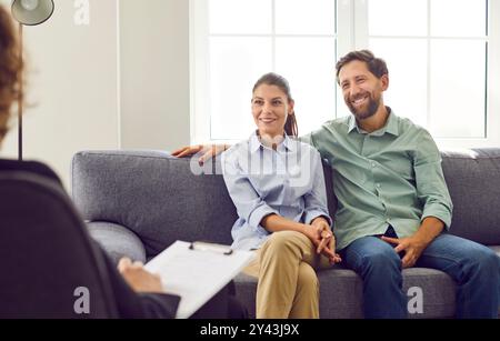 Jeune couple souriant assis sur le canapé et parlant avec le psychologue sur la séance de thérapie. Banque D'Images