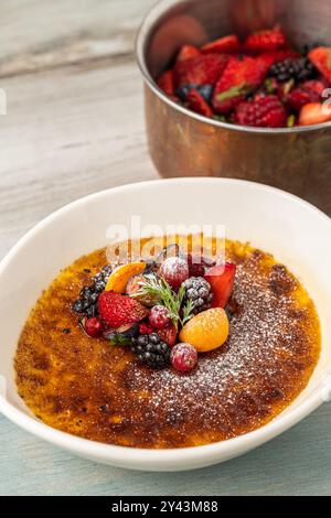 Crème brûlée décorée de fruits et de sucre en poudre sur une table en bois Banque D'Images