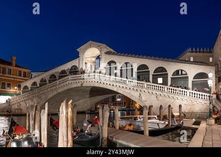 Venise, Italie - 20 mars 2024 - le pont du Rialto la nuit dans le centre-ville, passerelle en arc de pierre de 1591 à travers le Grand canal et gondoles Mo Banque D'Images