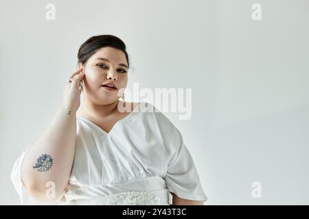 Une belle mariée plus grande taille présente sa robe de mariée et boucles d'oreilles, rayonnant l'élégance et la grâce. Banque D'Images