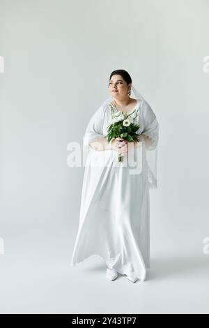 Une mariée magnifique se tient gracieusement, tenant un bouquet, exsudant la beauté dans sa robe exquise. Banque D'Images