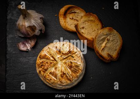 Brie ou camembert cuit au four sur fond noir avec du pain grillé ou des toasts et de l'ail. Photo de haute qualité Banque D'Images