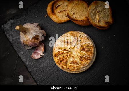 Brie ou camembert cuit au four sur fond noir avec du pain grillé ou des toasts et de l'ail. Photo de haute qualité Banque D'Images