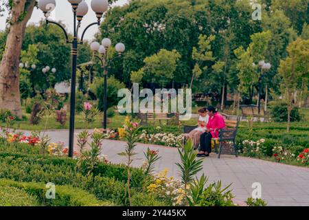 Deux femmes assises sur un banc dans un parc avec des fleurs autour d'elles Banque D'Images