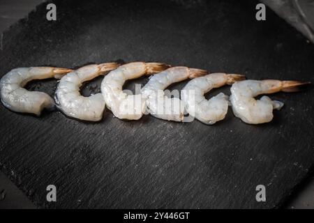 Crevettes de roi ou de tigre crues sur une planche de mica noir, disposées en rangée. Copyspace. Photo de haute qualité Banque D'Images