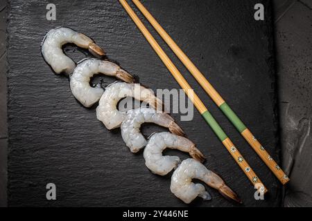 Crevettes de roi ou de tigre crues disposées dans une rangée avec des baguettes sur un panneau de mica noir, Copier l'espace. Photo de haute qualité Banque D'Images