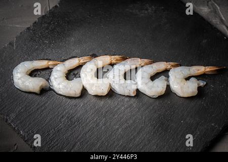 Crevettes de roi ou de tigre crues sur une planche de mica noir, disposées en rangée. Copyspace. Photo de haute qualité Banque D'Images