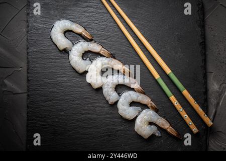 Crevettes de roi ou de tigre crues disposées dans une rangée avec des baguettes sur un panneau de mica noir, Copier l'espace. Photo de haute qualité Banque D'Images