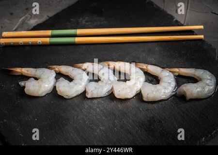 Crevettes de roi ou de tigre crues disposées dans une rangée avec des baguettes sur un panneau de mica noir, Copier l'espace. Photo de haute qualité Banque D'Images