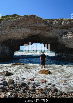 Personne debout dans l'océan regardant à travers la voûte rocheuse naturelle sur une plage. Banque D'Images