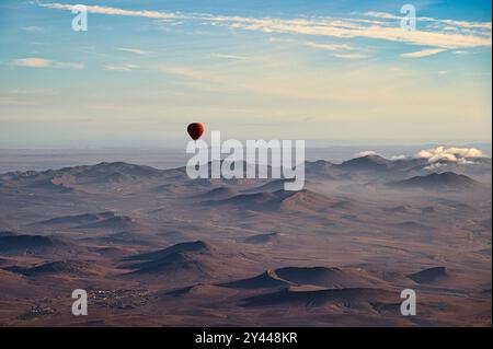 Une montgolfière rouge, flottant au-dessus du désert près de Marrakech, au Maroc par un clair jour de printemps, avec les montagnes de l'Atlas enneigées en arrière-plan Banque D'Images