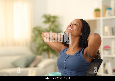 Femme noire heureuse se reposant sur une chaise à la maison Banque D'Images