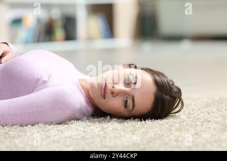 Femme apathique allongée sur le sol avec le regard perdu à la maison Banque D'Images