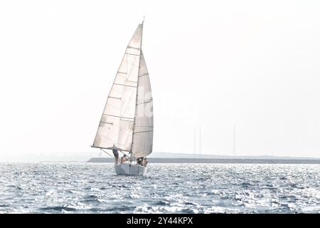 Voilier glissant gracieusement sur la mer sous un ciel nuageux, reflétant une scène sereine et idyllique parfaite pour les aventures estivales Banque D'Images