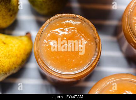 Une vue rapprochée d'un pot en verre rempli de confiture de poires maison lisse, entouré de poires fraîches mûres, mettant en évidence les ingrédients naturels et frais nous Banque D'Images