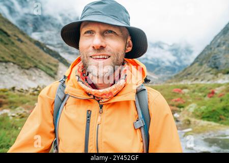 Portrait de Smiling Man avec sac à dos habillé veste imperméable orange et chapeau drôle marchant le chemin pendant le trek du parc national Makalu Barun au Népal. Banque D'Images