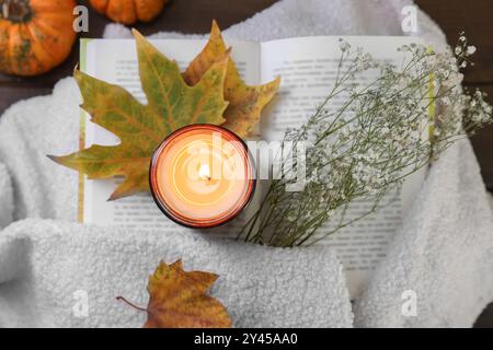 Bougie allumée, livre ouvert, chandail et décor d'automne sur la table, vue de dessus Banque D'Images