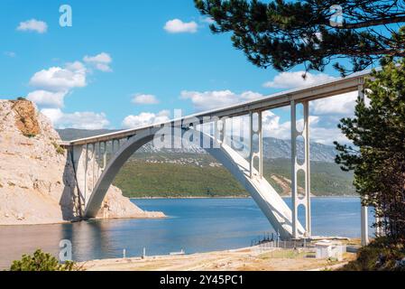 Pont en béton voûté enjambant un plan d'eau tranquille, sur fond de collines verdoyantes et de montagnes lointaines. Pont de Krk, Croatie. Banque D'Images