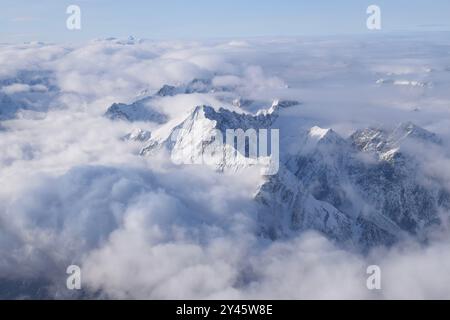 Vue aérienne à couper le souffle de la chaîne de montagnes alpine enneigée culminant à travers de lourds nuages. Sommets des Alpes de Ötztal depuis une fenêtre d'avion. Banque D'Images