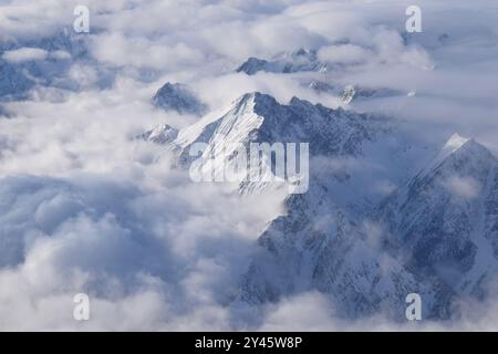 Vue aérienne à couper le souffle de la chaîne de montagnes alpine enneigée culminant à travers de lourds nuages. Sommets des Alpes de Ötztal depuis une fenêtre d'avion. Banque D'Images