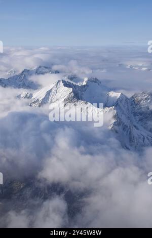 Vue aérienne à couper le souffle de la chaîne de montagnes alpine enneigée culminant à travers de lourds nuages. Sommets des Alpes de Ötztal depuis une fenêtre d'avion. Banque D'Images