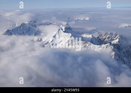 Vue aérienne à couper le souffle de la chaîne de montagnes alpine enneigée culminant à travers de lourds nuages. Sommets des Alpes de Ötztal depuis une fenêtre d'avion. Banque D'Images