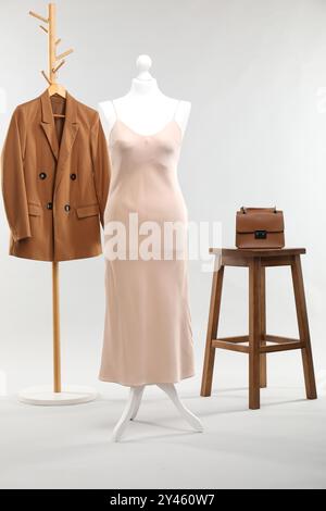 Un mannequin féminin avec robe, rack avec veste, tabouret et sac sur fond clair Banque D'Images