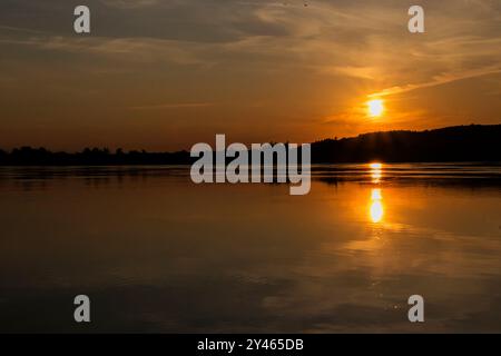 Tandis que le soleil descend lentement vers l'horizon, il projette une lueur chaude sur le plan d'eau tranquille, créant une scène à couper le souffle Banque D'Images