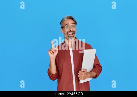 Homme d'affaires mi-âgé excité pointant le doigt tenant l'ordinateur portable isolé sur bleu. Banque D'Images