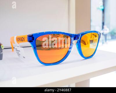 Les lunettes de soleil bleues avec des verres orange reposent sur une étagère blanche à l'intérieur d'un magasin, reflétant les lumières intérieures et la rue à l'extérieur Banque D'Images