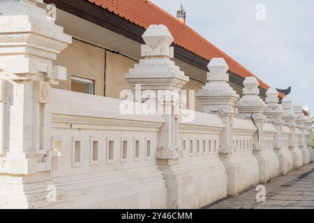 Un mur de pierre avec des piliers décoratifs et une porte, menant à un chemin. Le mur présente des sculptures complexes et est placé sur une toile de fond d'un nuageux Banque D'Images