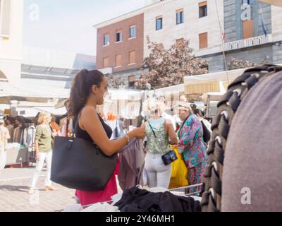 Cremona, Italie 31 août 2024 Une femme choisit des vêtements d'un porte-vêtements sur un marché en plein air avec d'autres personnes faisant du shopping en arrière-plan Banque D'Images