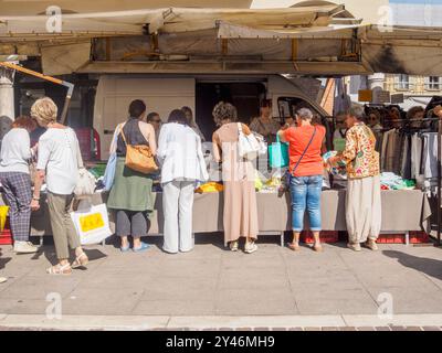 Cremona, Italie 31 août 2024 clients naviguant et achetant des vêtements dans un étal sur un marché de vêtements de plein air dans une ville italienne par un été ensoleillé Banque D'Images