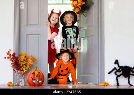 Les enfants trichent ou gâtent le soir d'Halloween. Les enfants habillés à la porte de la maison décorée. Garçon et fille en costume de sorcière et de vampire et chapeau Banque D'Images