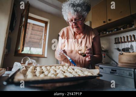 Femme âgée préparant des pâtisseries maison dans un cadre de cuisine rustique Banque D'Images