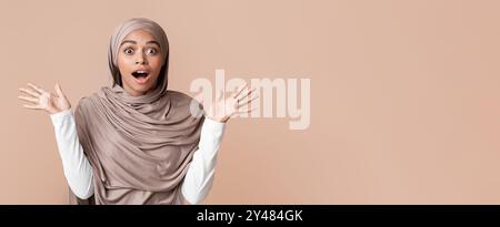 Surprise femme afro musulmane en foulard levant les mains sous le choc Banque D'Images